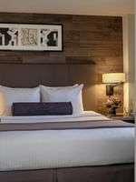 View through white french doors of a bed with a bolster by a bedside lamp in Premier Suite at Warwick Denver