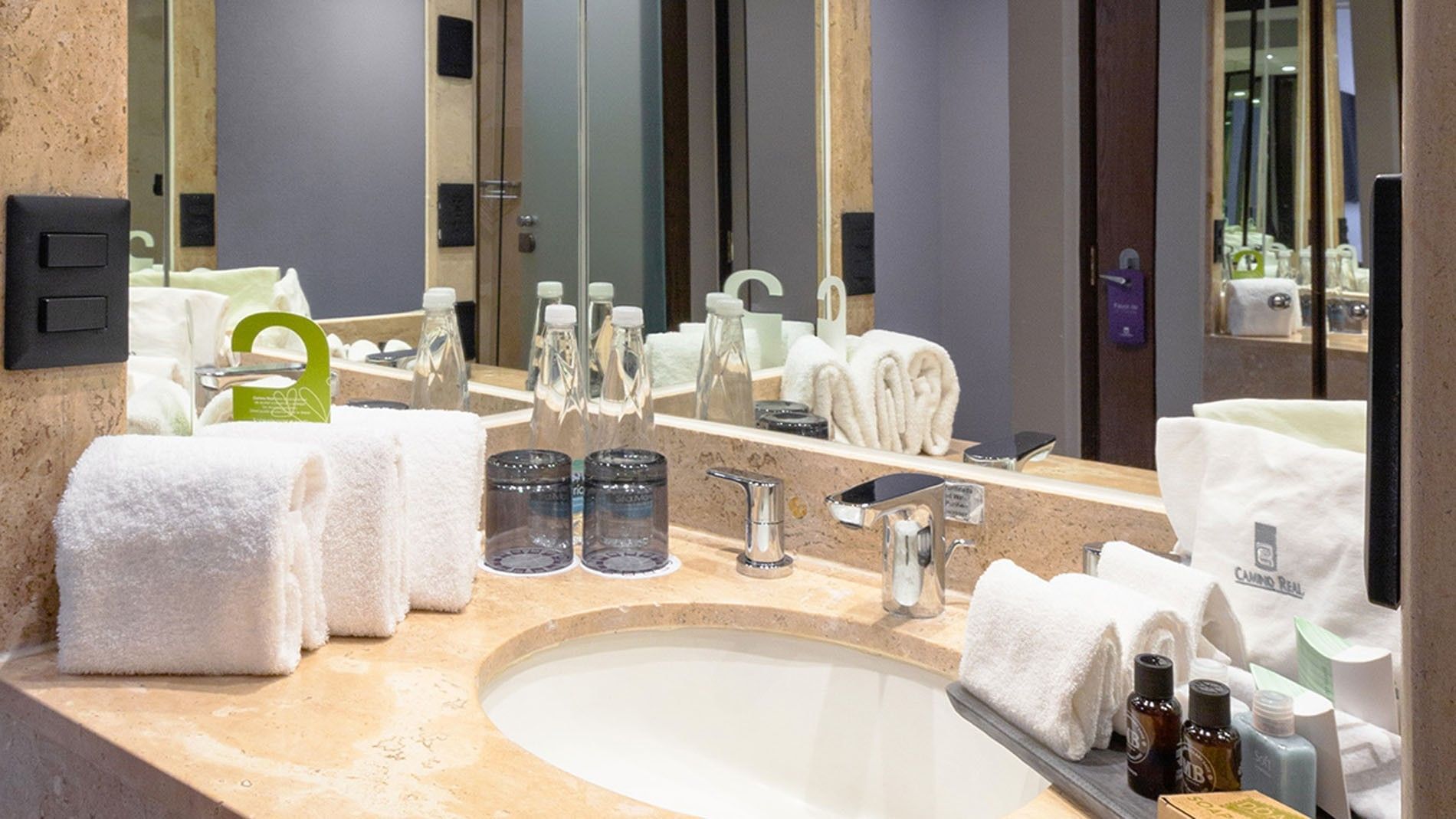 King Deluxe Superior bathroom vanity with white towels bottled water and glass cups at Camino Real Aeropuerto Mexico