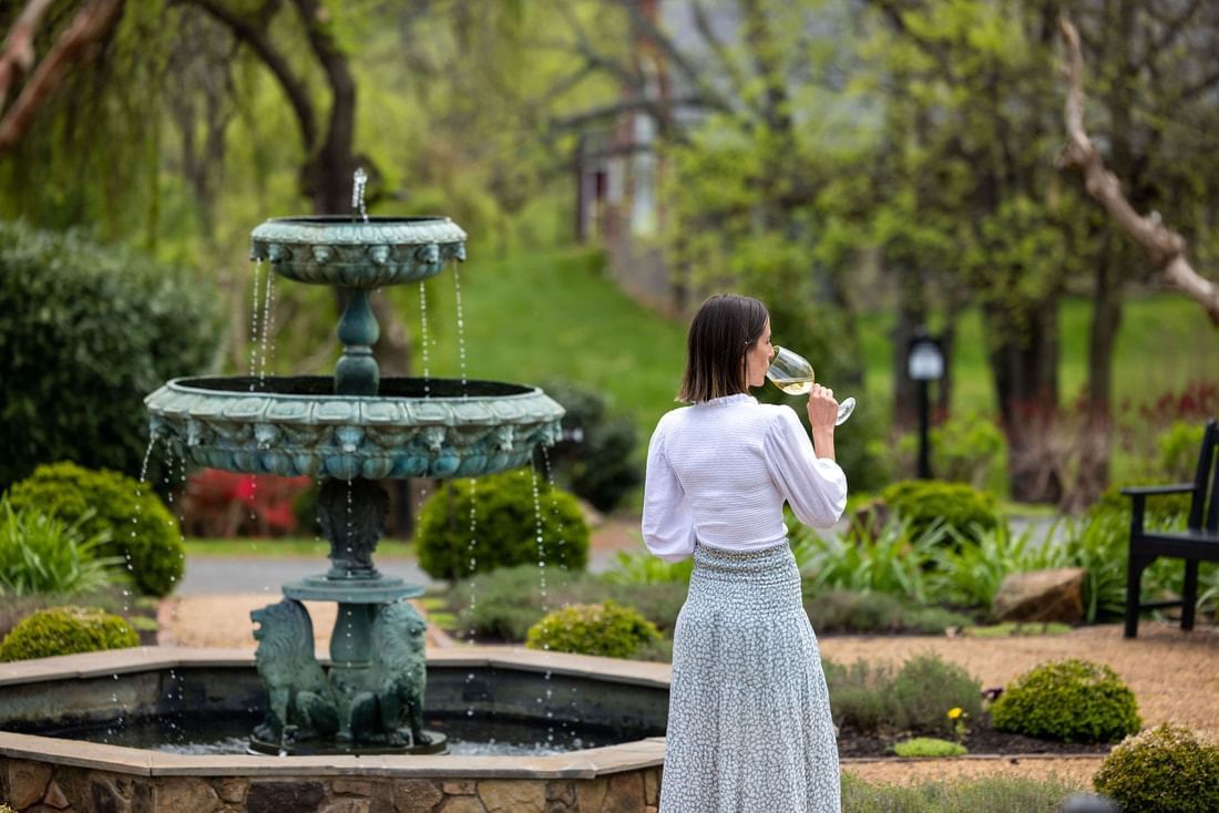 Lady sipping on wine by a fountain in the Inn at Willow Grove Garden