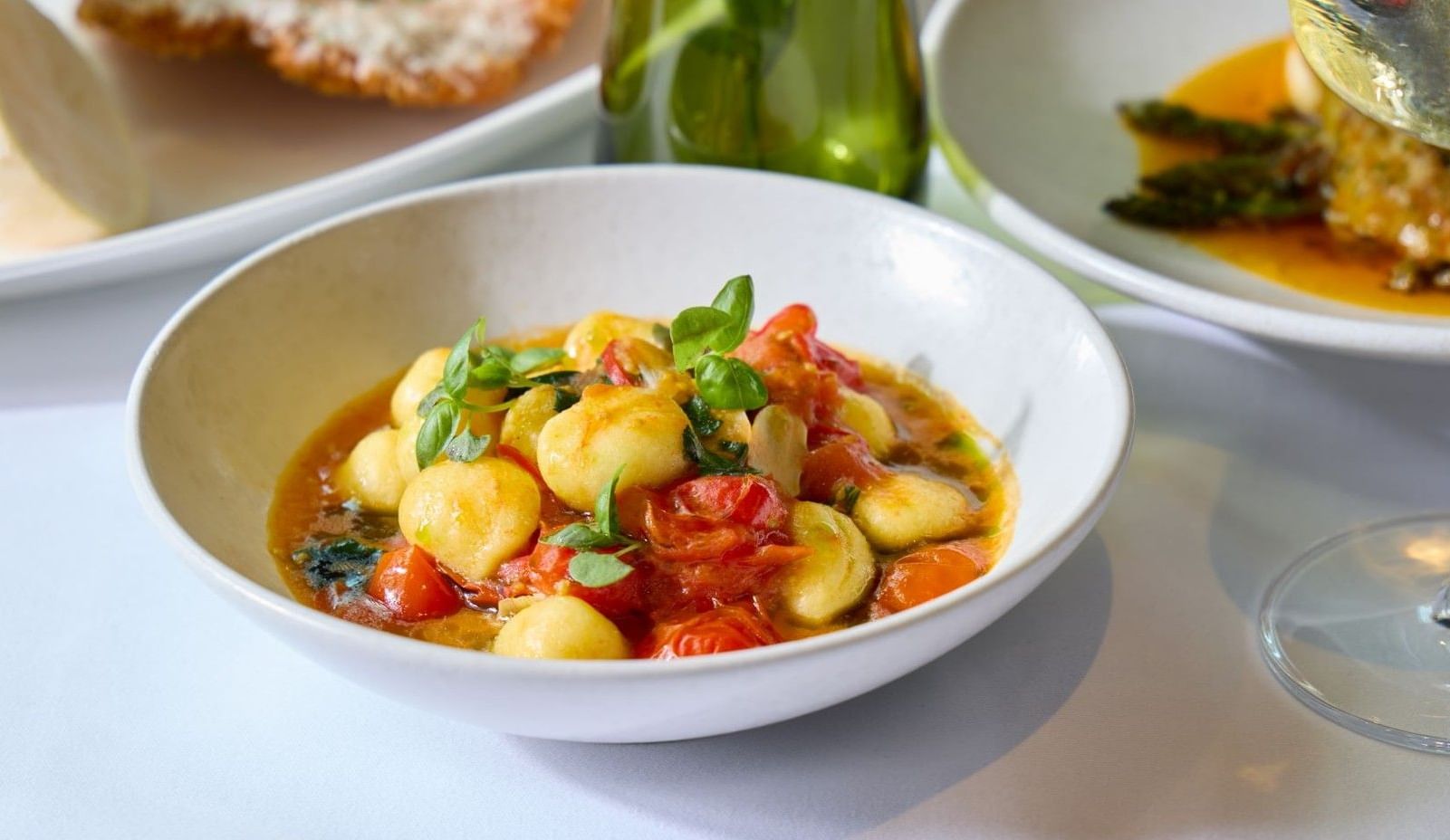 Gnocchi in tomato sauce with basil beside white wine glass and gourmet Italian dining dishes at The Londoner Hotel