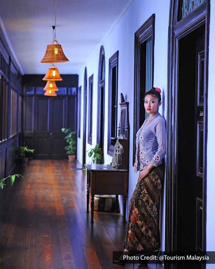 A woman styled in Nyonya Kebaya stands beside the corridor - Lexis Suites Penang