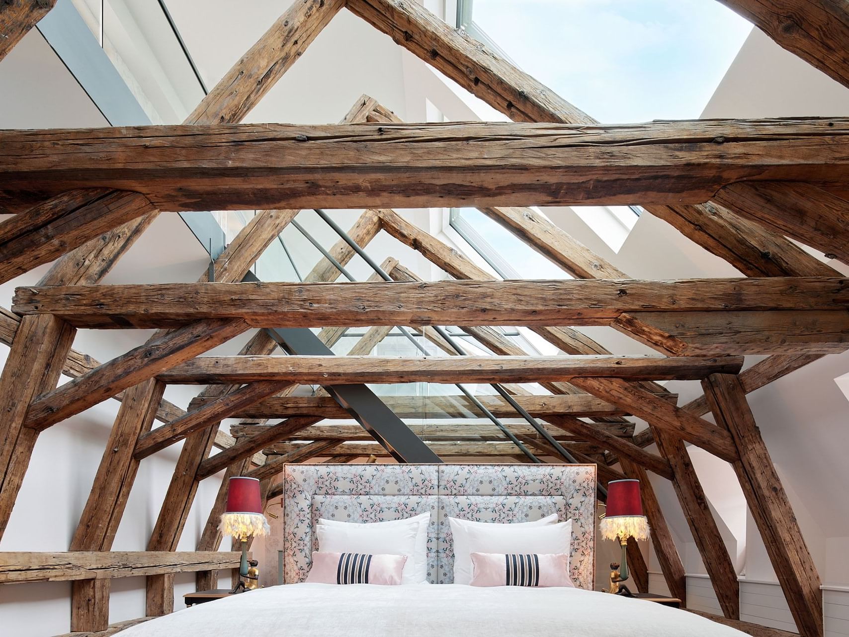Leopold Suite with exposed wooden beams, glass skylight, and a bed with pink and white striped pillows.