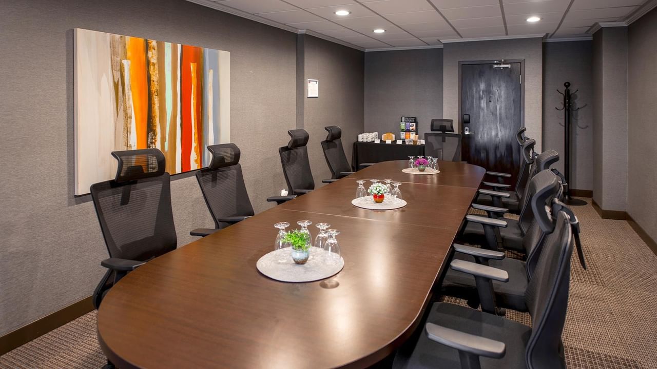 Modern conference room with oval table, ergonomic chairs, and colorful abstract art at Coast Calgary University Area Hotel by APA.