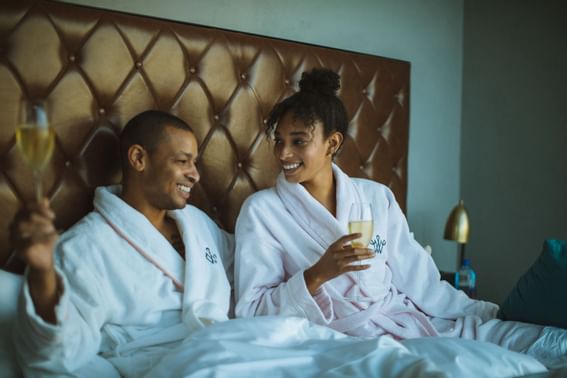 A couple with their smiling face lying in their bed holding the glass of champagne