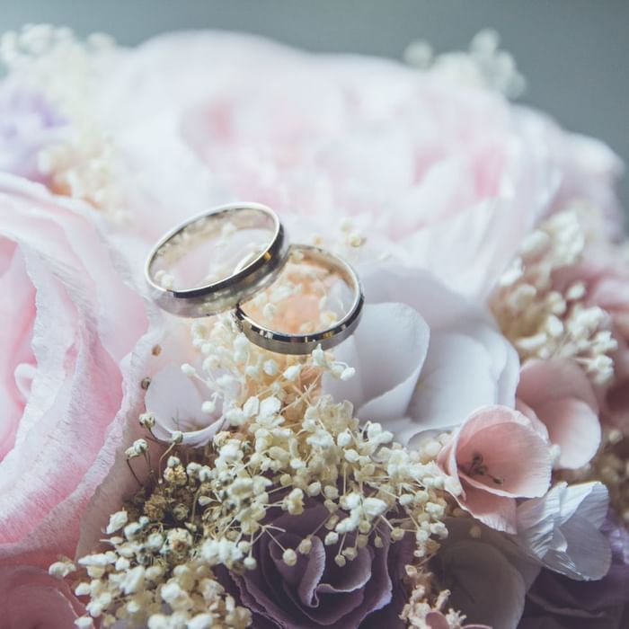 Due anelli di nozze d'argento su un bouquet di fiori rosa e bianchi.