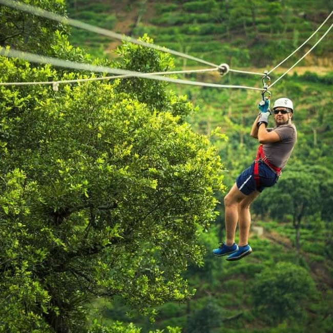 Person zip-lining through lush green forest canopy wearing safety helmet and harness on an outdoor adventure course at Go Ape Bracknell.