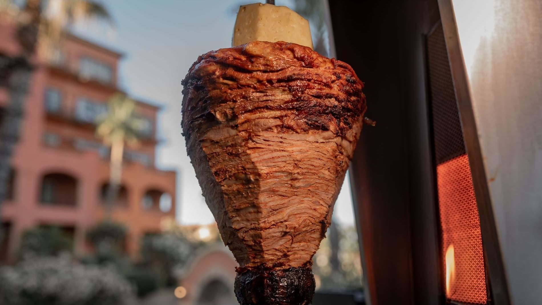 Spit-grilled meat for tacos al pastor cooking outdoors in front of a resort building in Tahona at Hacienda del Mar Los Cabos.