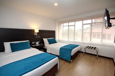 Twin Dann Cali featuring two beds with teal accents, a modern design, and large windows at Dann Carlton Cali