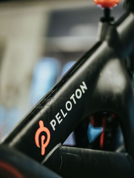 Detailed view of the white Peloton logo in a fitness area, near blue lighting on a matte black bike at Elysium Manly