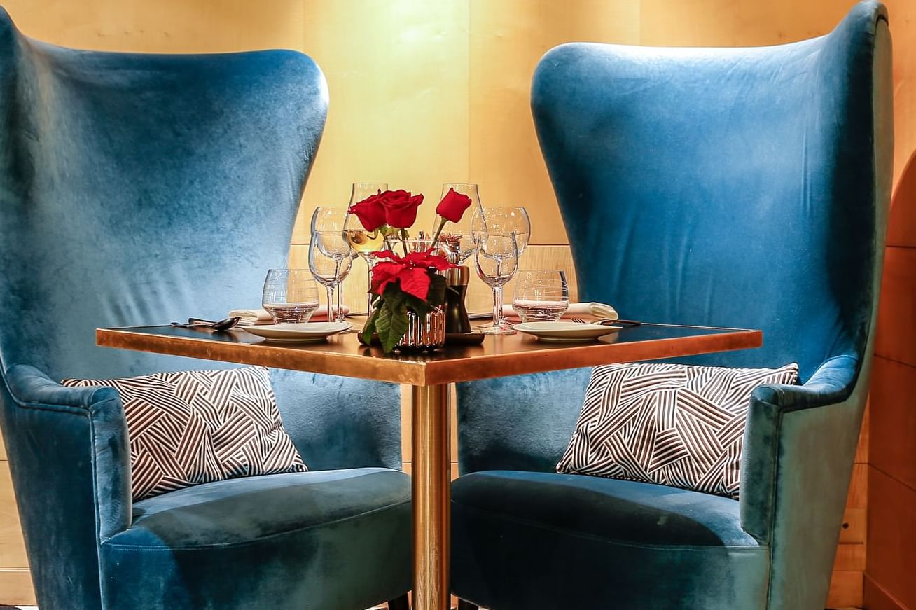 Two blue velvet chairs, a small table set with wine glasses and roses in Restaurant-Le W