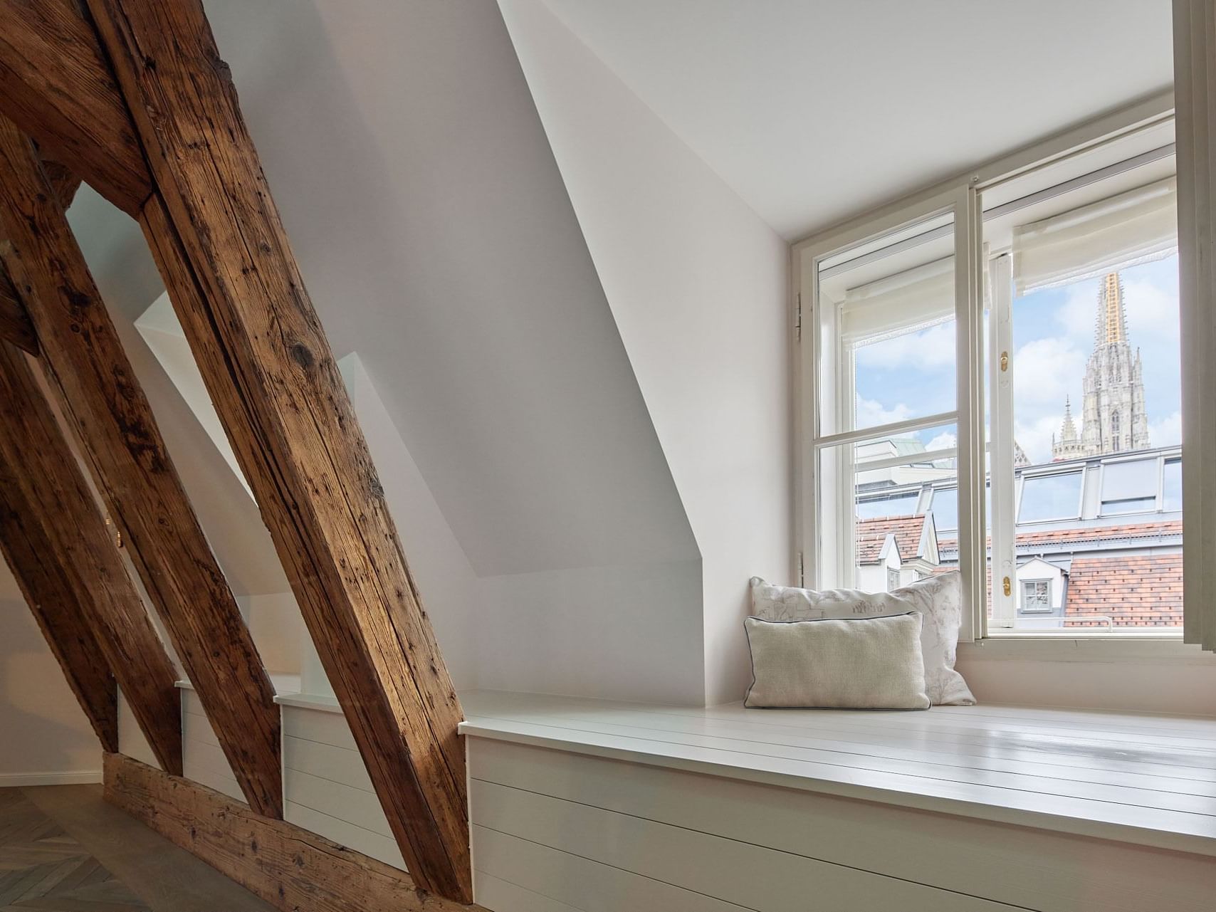 Wooden beams and a white bench with pillows near a large window.