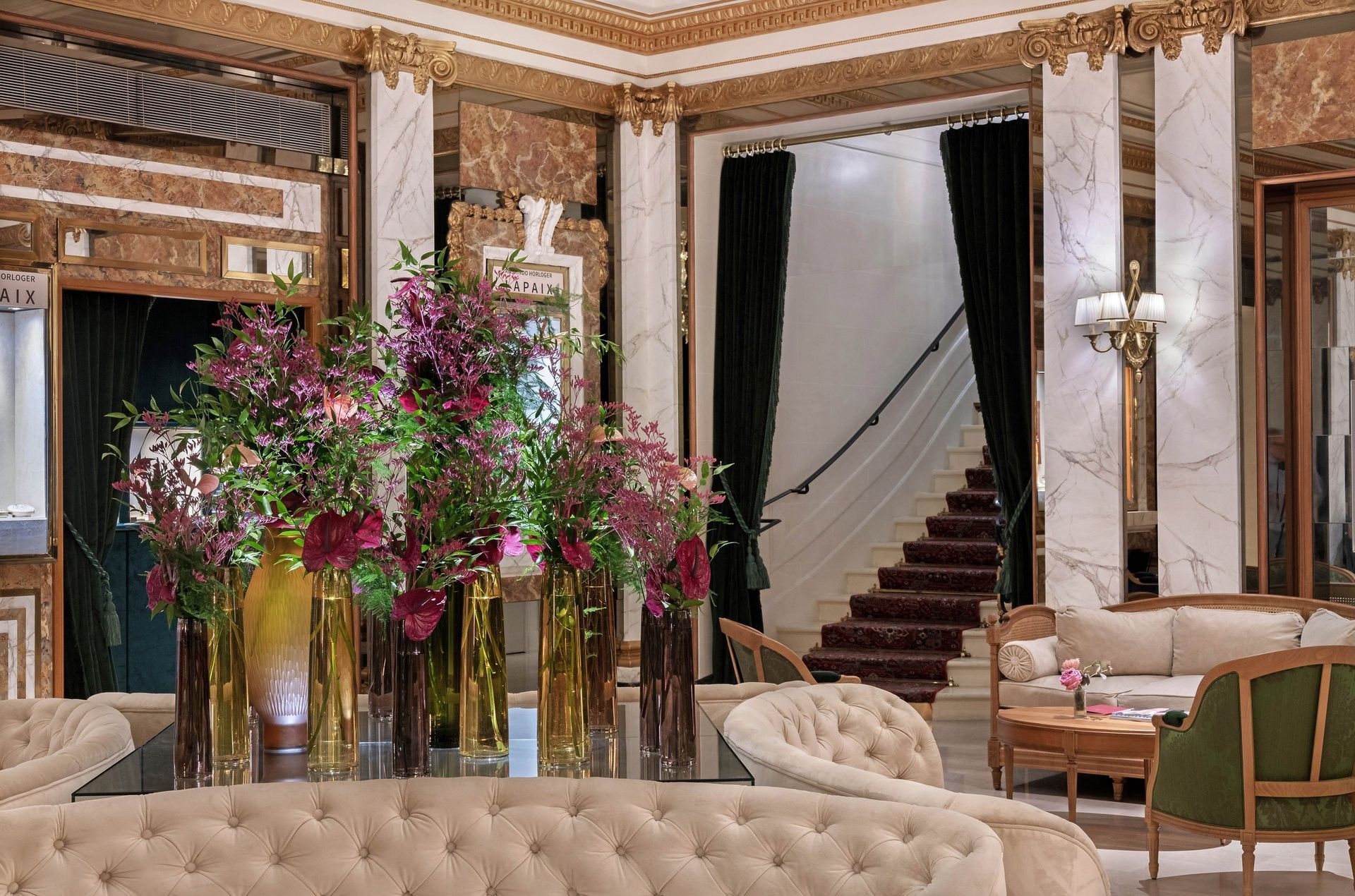 Tall floral arrangements in glass vases on a mirrored table, surrounded by velvet chairs at Hotel Westminster Paris
