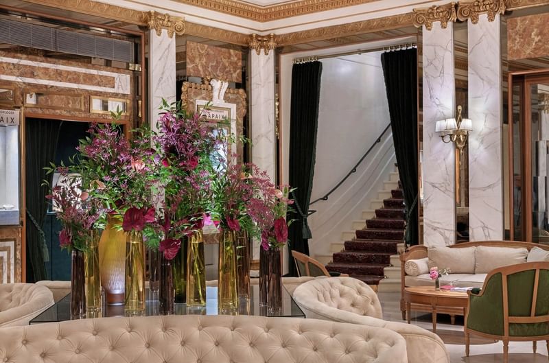 Hall d'hôtel luxueux avec colonnes en marbre, escalier élégant et compositions florales roses à Hotel Westminster Warwick Paris