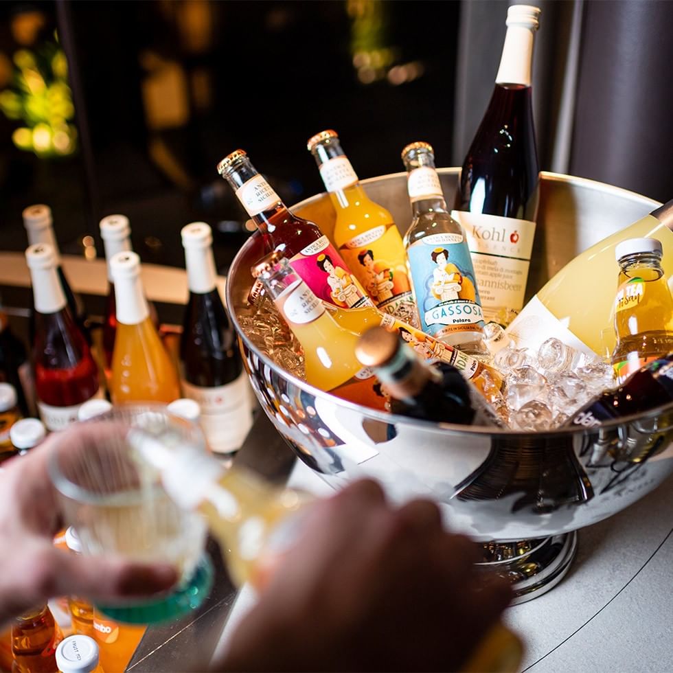 Hände füllen ein Glas mit Getränken aus silbernem Eimer voller Eis und Flaschen.