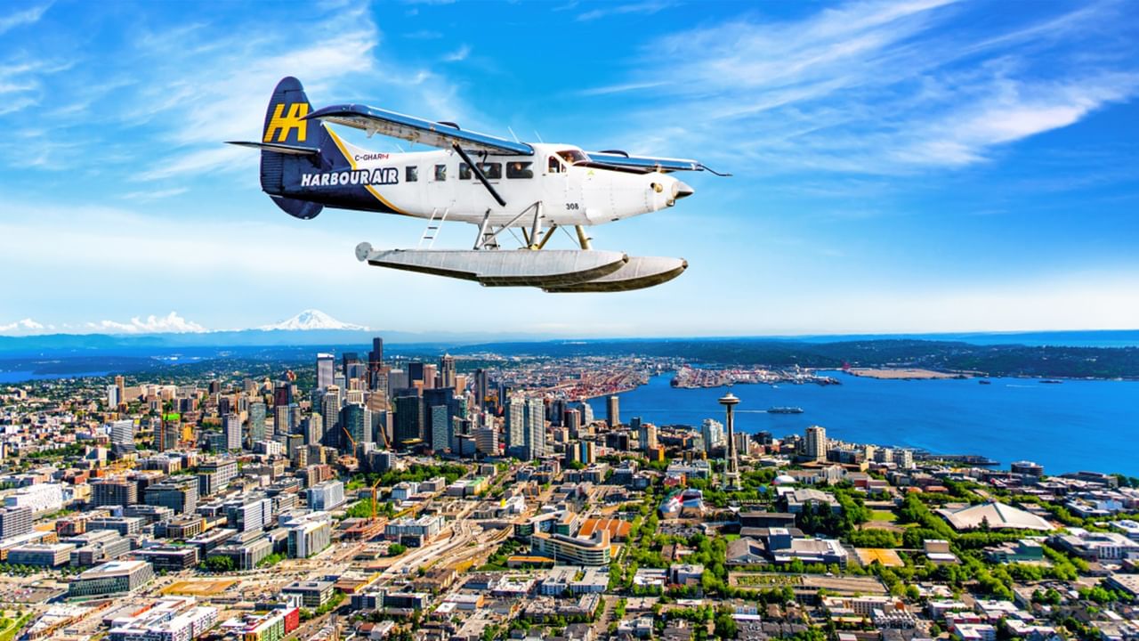 Harbour Air seaplane flying above a cityscape with buildings and water below.