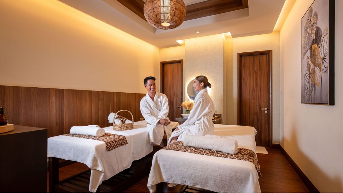Happy couple in white robes sitting on massage beds in a spa treatment room at Sunway Resort