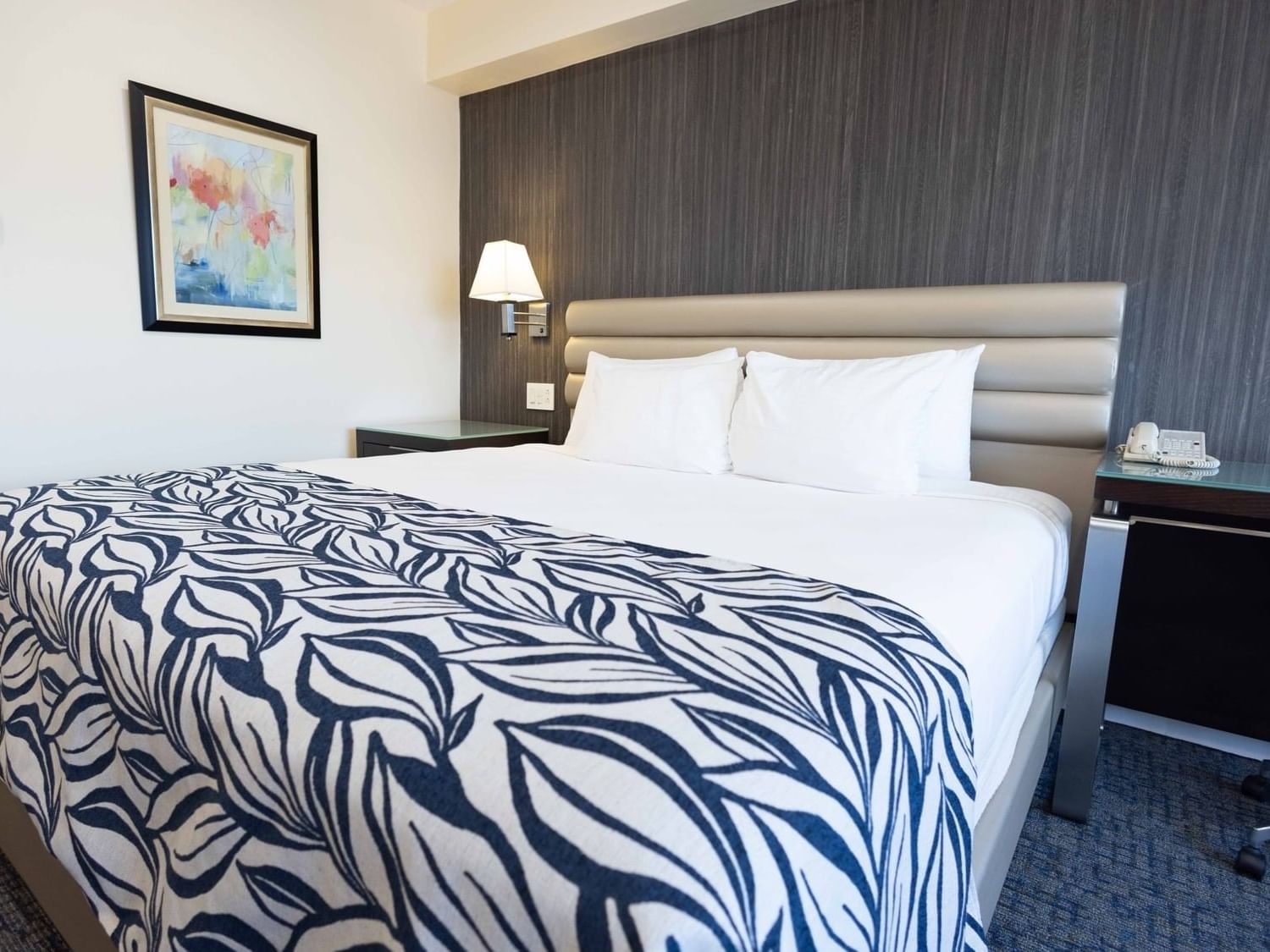 Modern bed with leaf-pattern throw blanket beside a nightstand & framed artwork in Deluxe King Room at Jamaica Pegasus Hotel