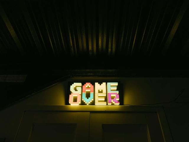 A glowing GAME OVER sign in retro pixel art style hangs above Game Zone door at El Conquistador Resort