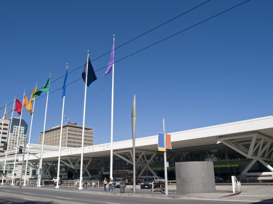 Multiple flags on poles in front of the white Yosemite Center building under a clear blue sky.