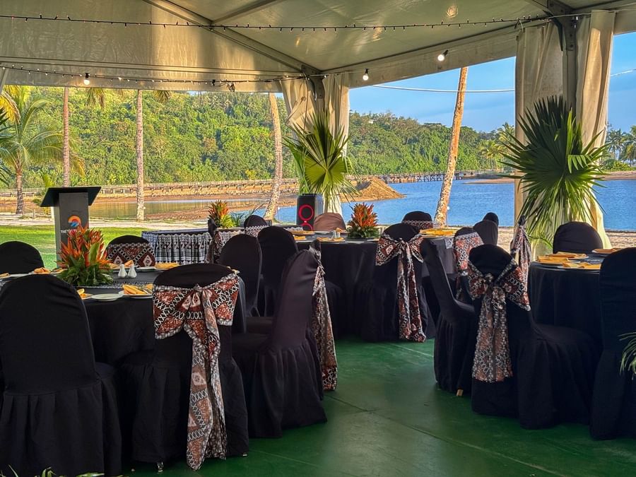 Tables and chairs set up under a canopy with water and palm trees view at The Naviti Resort.