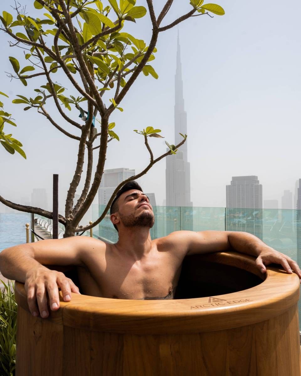 Man stepping into a refreshing wooden plunge pool on a rooftop at Paramount Hotel Midtown, with a Dubai skyline view
