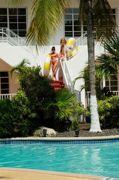 Couple descending the outdoor staircase with yellow and white pool floats, heading to the pool at Tradewinds Apartment Hotel