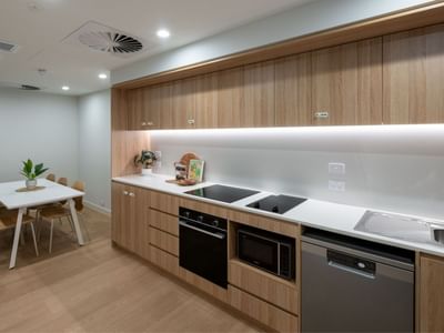 Modern kitchen with wooden cabinets, white countertops, dining table, and appliances at UniLodge Brisbane City.