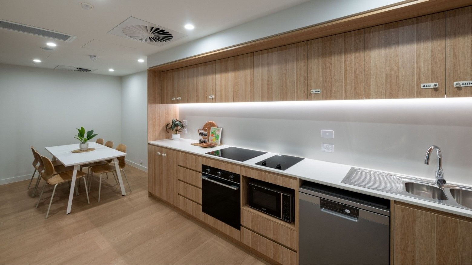 Modern kitchen with wooden cabinets, white countertops, dining table, and appliances at UniLodge Brisbane City.