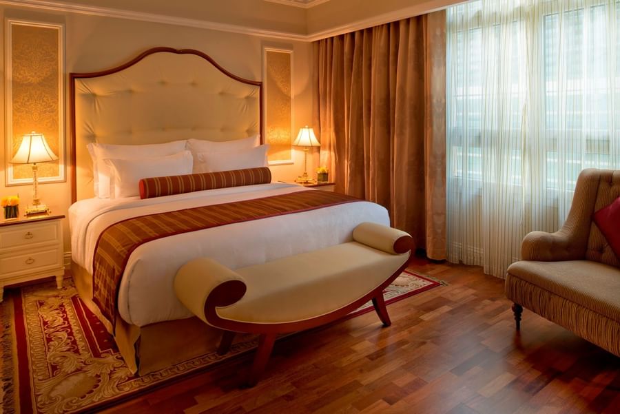 Cream bench by a king bed under a tufted headboard on a red patterned rug in Superior Room at Warwick Doha Hotel