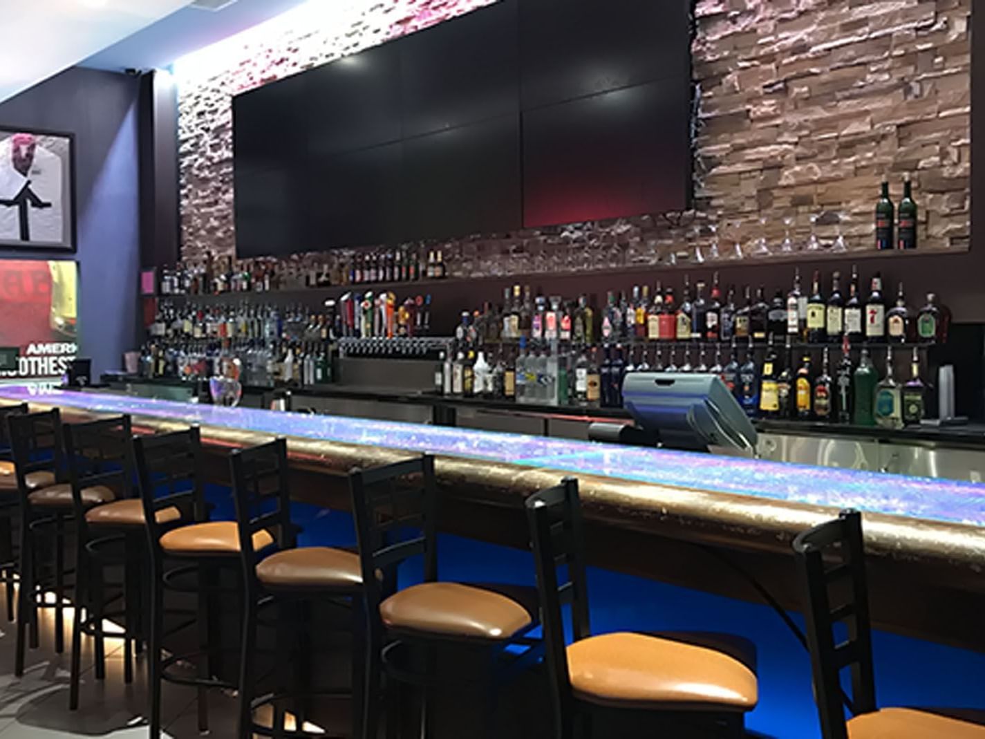 Empty bar with blue lighting, numerous liquor bottles, framed pictures, and a long counter.