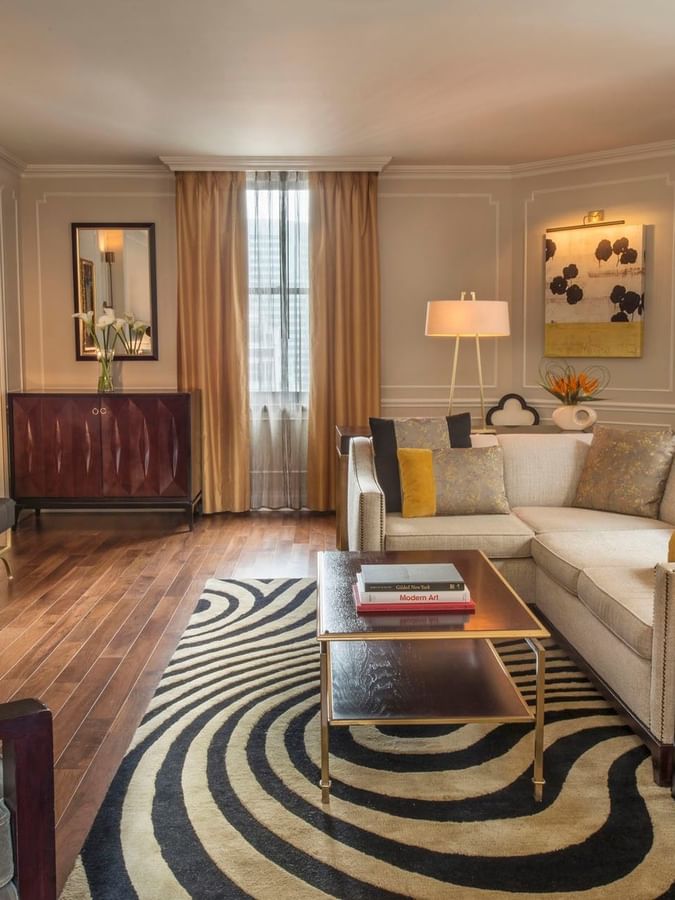 Wirl-patterned rug with cream sectional sofa facing TV screen and a warm fireplace in Jane Suite at Warwick New York 