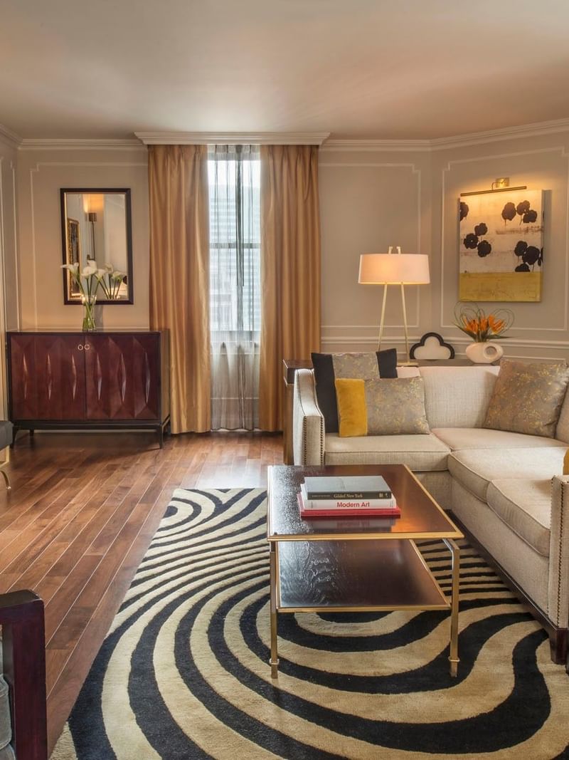 Wirl-patterned rug with cream sectional sofa facing TV screen and a warm fireplace in Jane Suite at Warwick New York 