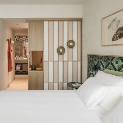 Camera da letto con letti bianchi, tavolino, sedie verdi, lampada e bagno con specchio.