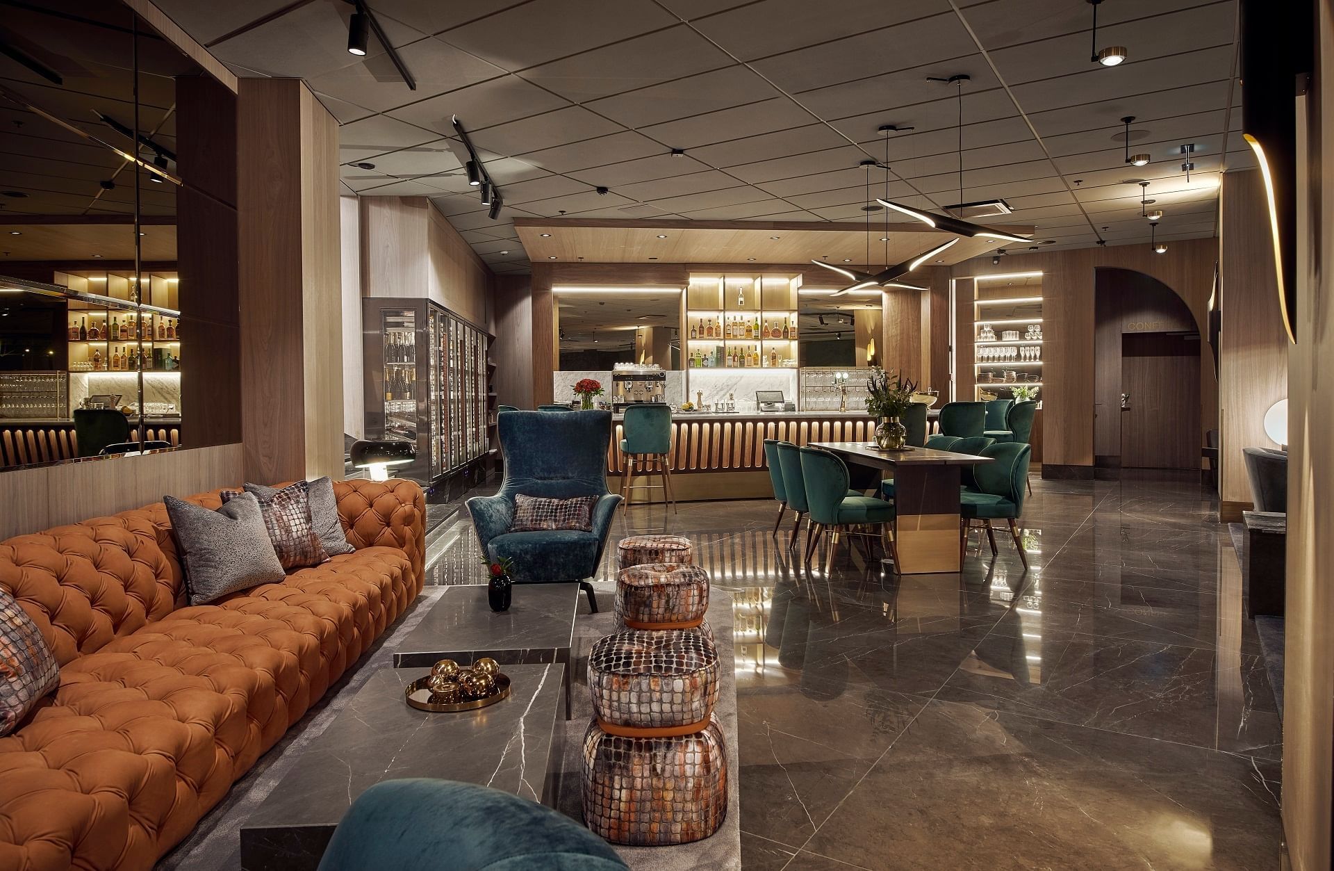 A luxurious lounge area with a large Baxter couch, green chairs, a dining table, and a bar with shelves.