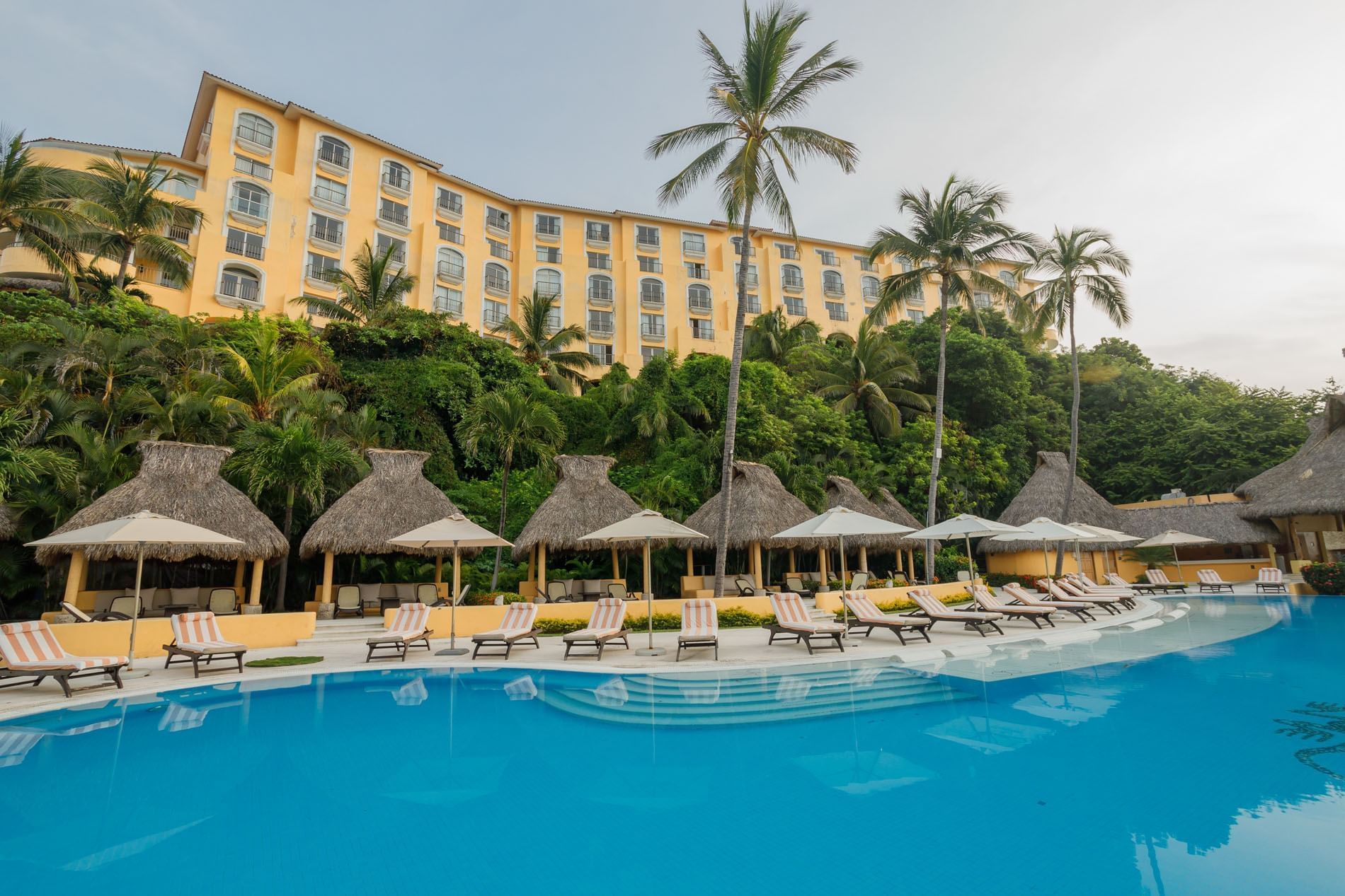 Luxury pool area featuring striped loungers, palapas, and a hillside hotel wing at Quinta Real Acapulco