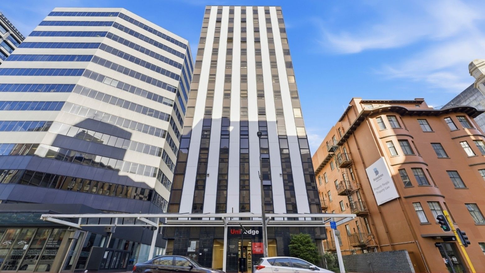 Tall modern UniLodge building among other urban structures under a clear blue sky.