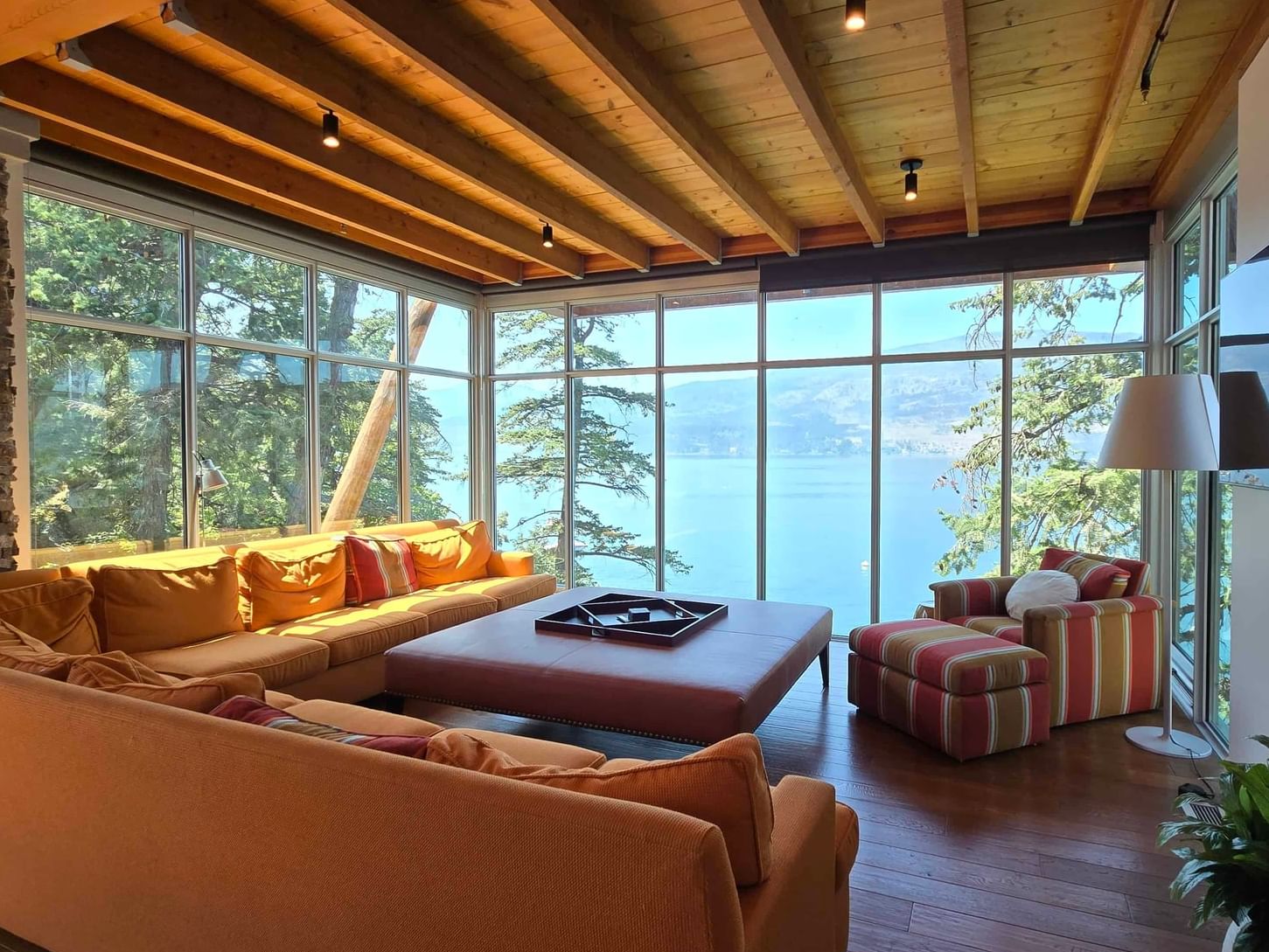 Living room with large windows, wooden ceiling, and lake view, with couches, table, and plant.