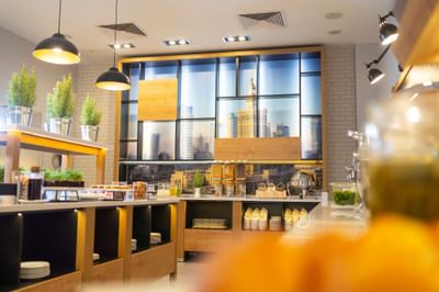 Restaurant interior with large windows, industrial style lighting and food counter in Warsaw at Metropol Hotel