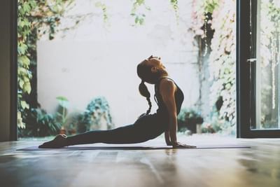 Guest practicing yoga by a large window under hanging vines in the wellness studio at Ellipse Grace Bay
