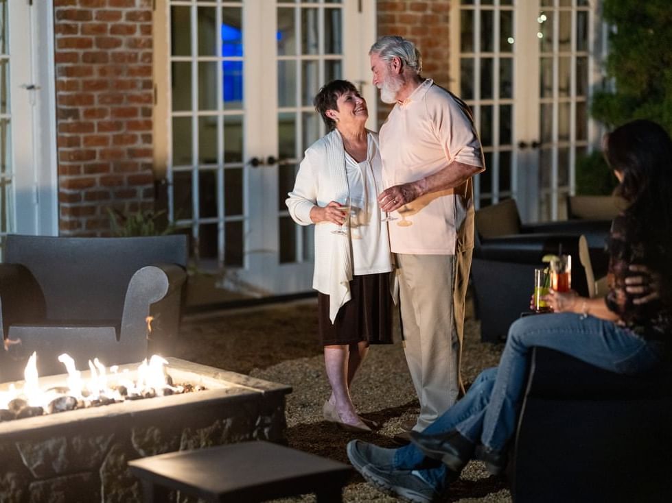 Two people converse by a fire pit, with another seated nearby, in the Inn at Willow Grove