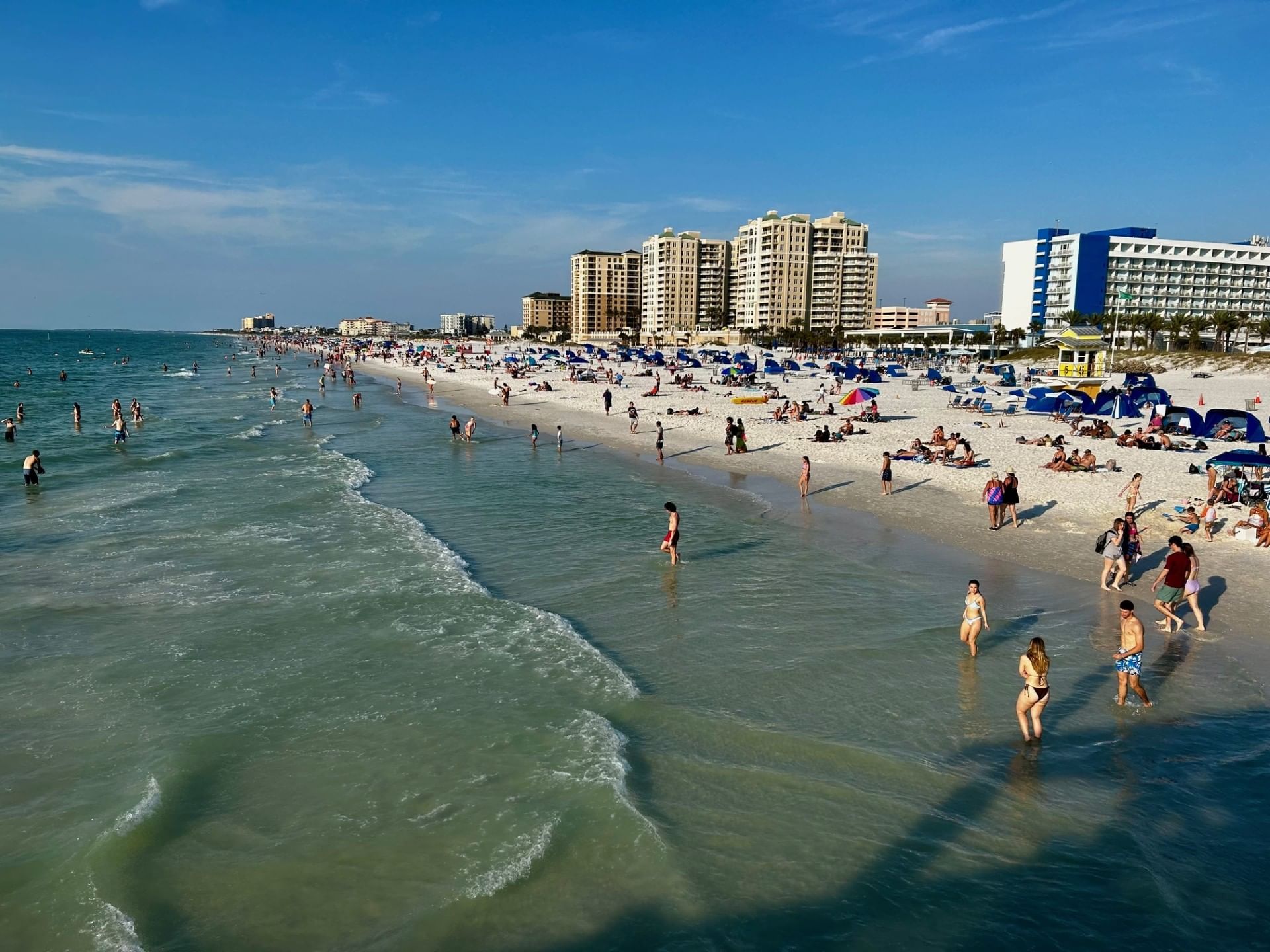 A beach with tall buildings and people on the sand and in the water.