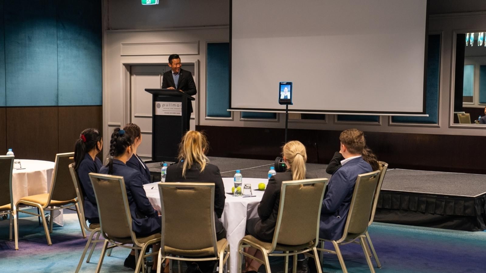 A man standing at a podium with a group of people sitting around it at Pullman King George Square