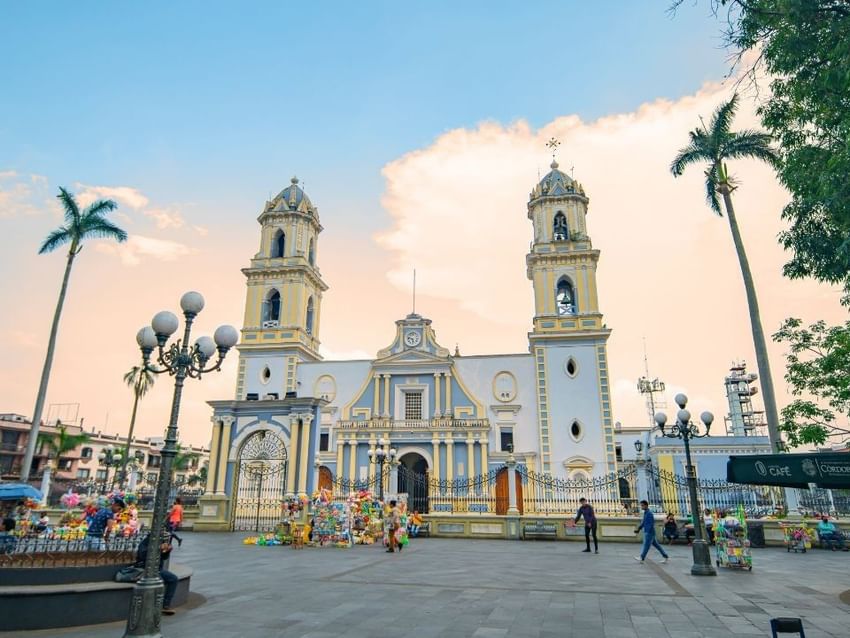 People walking in a plaza in front of a blue and white church near Camino Real Hotels