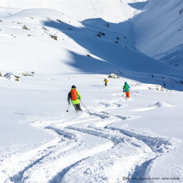 Drei Skifahrer navigieren durch eine schneebedeckte Berglandschaft, mit Spuren im Schnee.