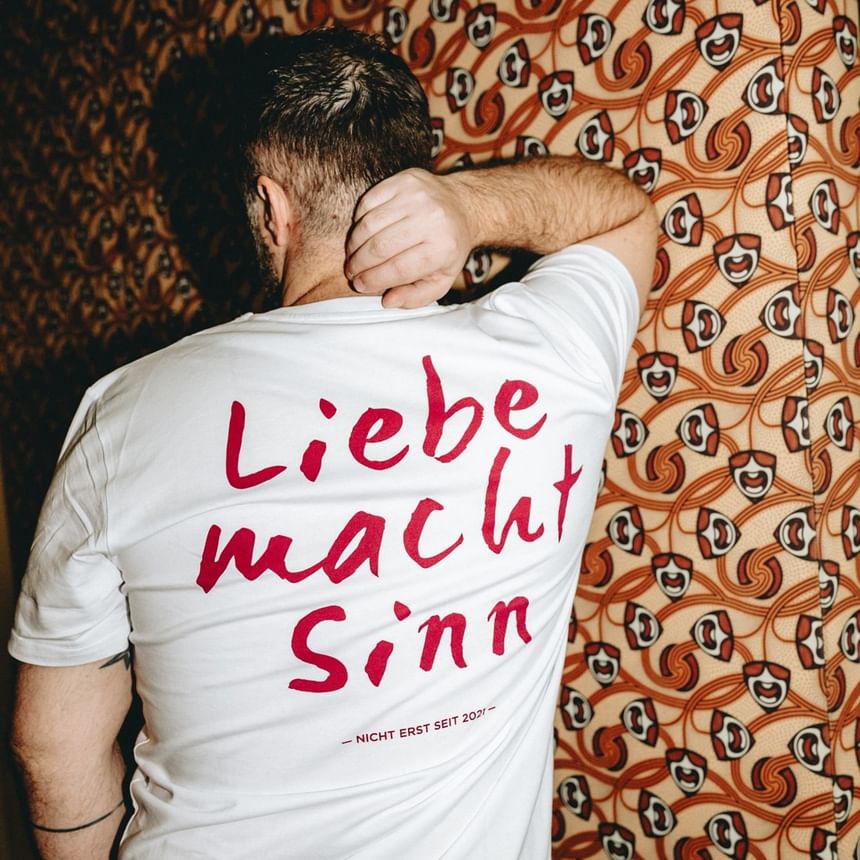 Mann mit weißem T-Shirt und rotem Aufdruck vor Mustertapete im Hotel Motto