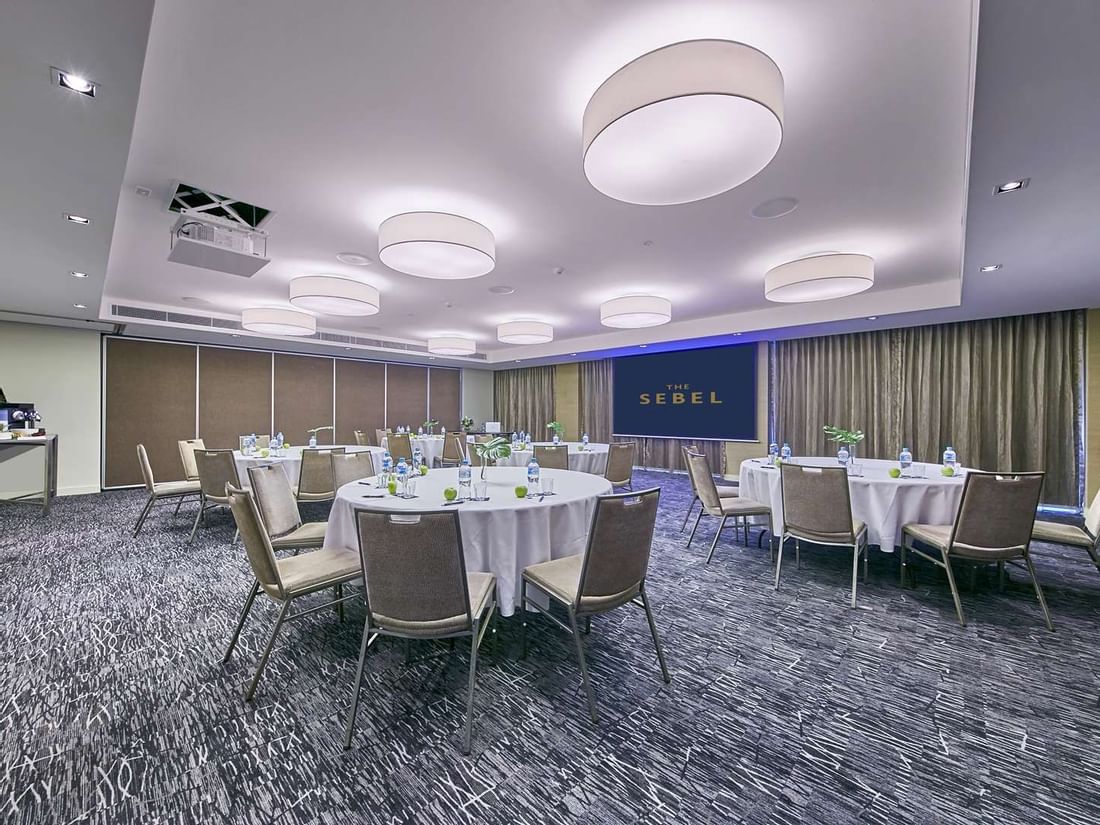 Conference room set up for a round table event with a projector screen in the background at The Sebel Mandurah