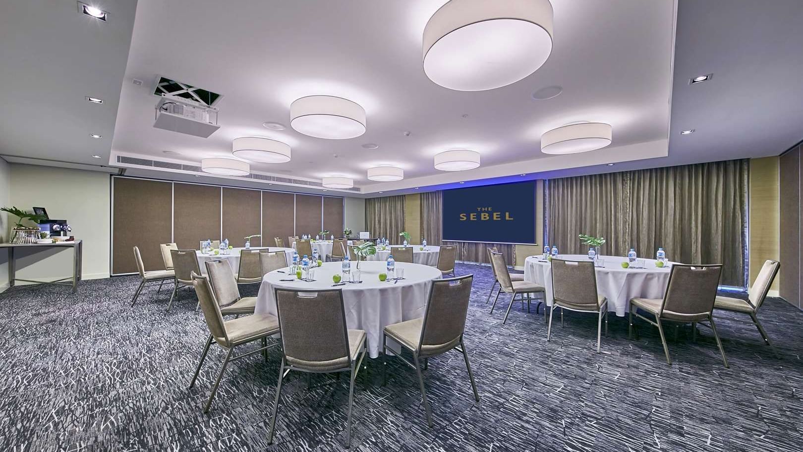 Conference room set up for a round table event with a projector screen in the background at The Sebel Mandurah