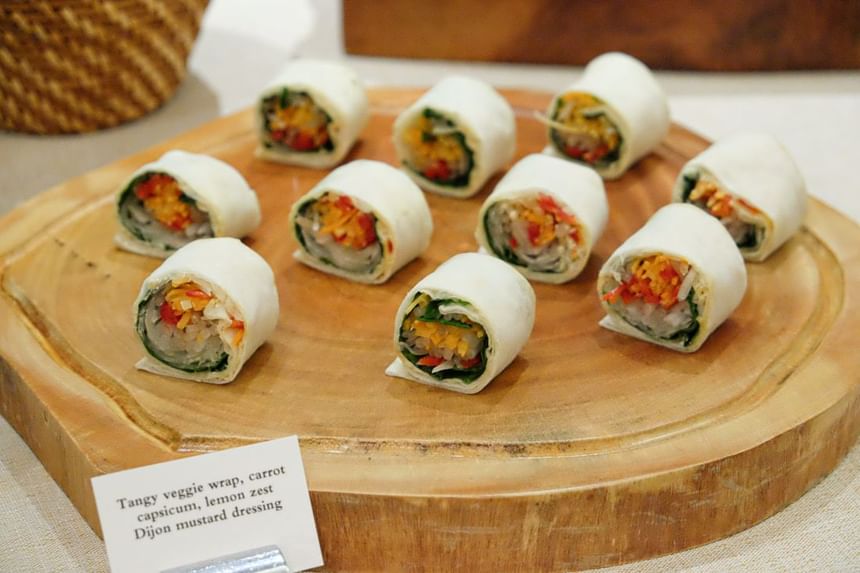 Wooden platter displays neatly sliced veggie wraps filled with colorful carrots, capsicum, and greens at Park Hyatt Saigon