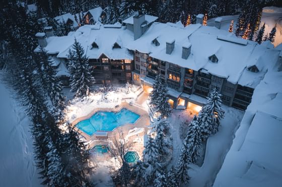 Illuminated top view of the hotel buildings and outdoor pool surrounded by snowy forest at Blackcomb Springs Suites