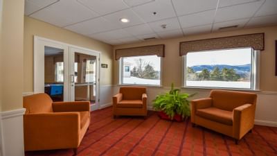 Fox Ridge Resort lobby room with three orange chairs, and windows showing a snowy landscape with trees and mountains.